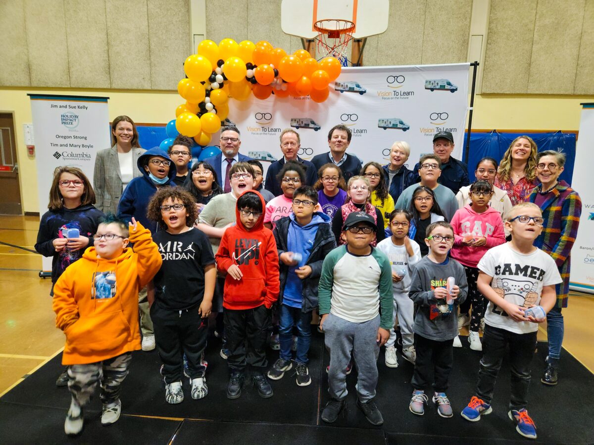 A group of elementary school students pose for a photo with Vision To Learn founder Austin Beutner, New York Times columnist Nick Kristof, Jim & Sue Kelly, and representatives from Portland Public Schools and Warby Parker.