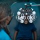 A child in a dark blue polo shirt sits in an optometry chair and looks through a phoropter.