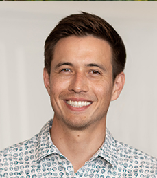 A man in a patterned dress shirt stands in front of a white background.