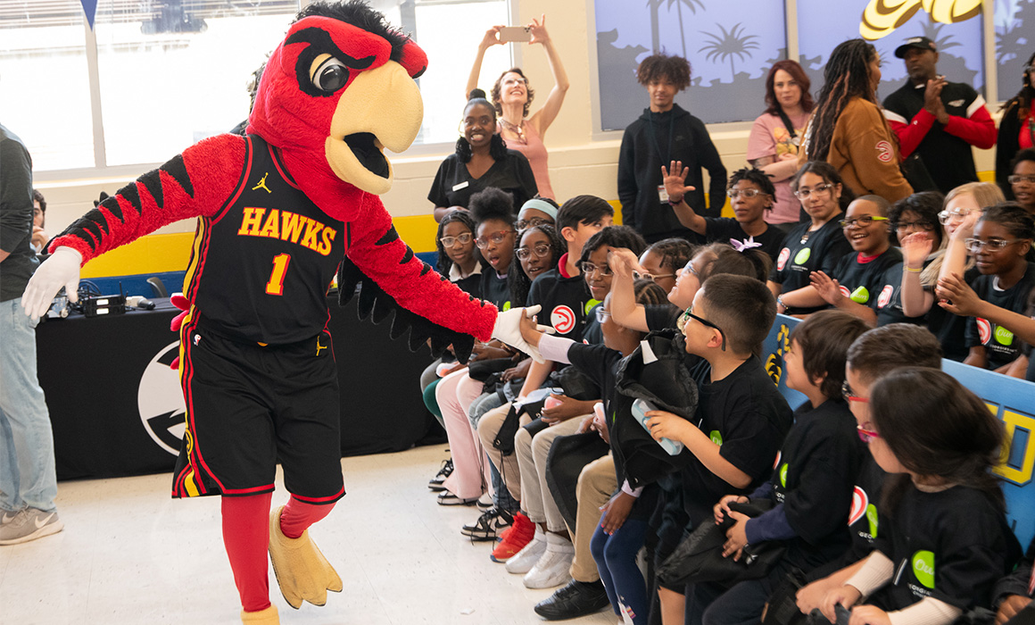 A large red hawk mascot wearing an Atlanta Hawks jersey, with the number one printed on it, runs past a group of students while giving them high fives.