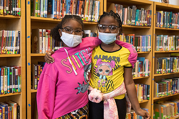 Two elementary school students pose together in front of a book shelf.