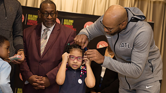 Vince Carter of the Atlanta Hawks helps a student with her new glasses while Dr. Stephen Green, Superintendent of DeKalb County Schools, looks on. Toney Elementary, December 10, 2018, Atlanta, GA.