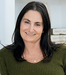 A woman wearing a green sweater stands in front of a white background.