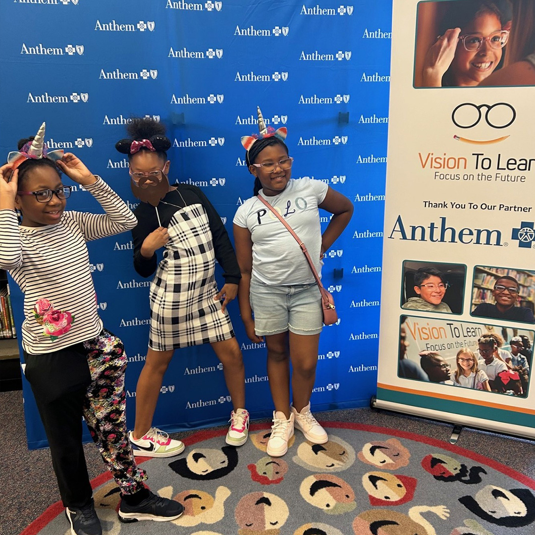 Three elementary school students stand in front of a blue step and repeat adorned with Anthem Blue Cross Blue Shield's logo.