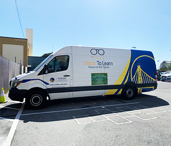 A Vision To Learn clinic adorned in a Golden State Warriors wrap is parked in a school's parking lot.
