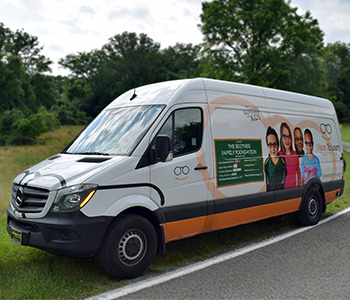 A white sprinter van adorned with the Vision To Learn logo, and decals of a chalkboard, glasses and a group of four kids.