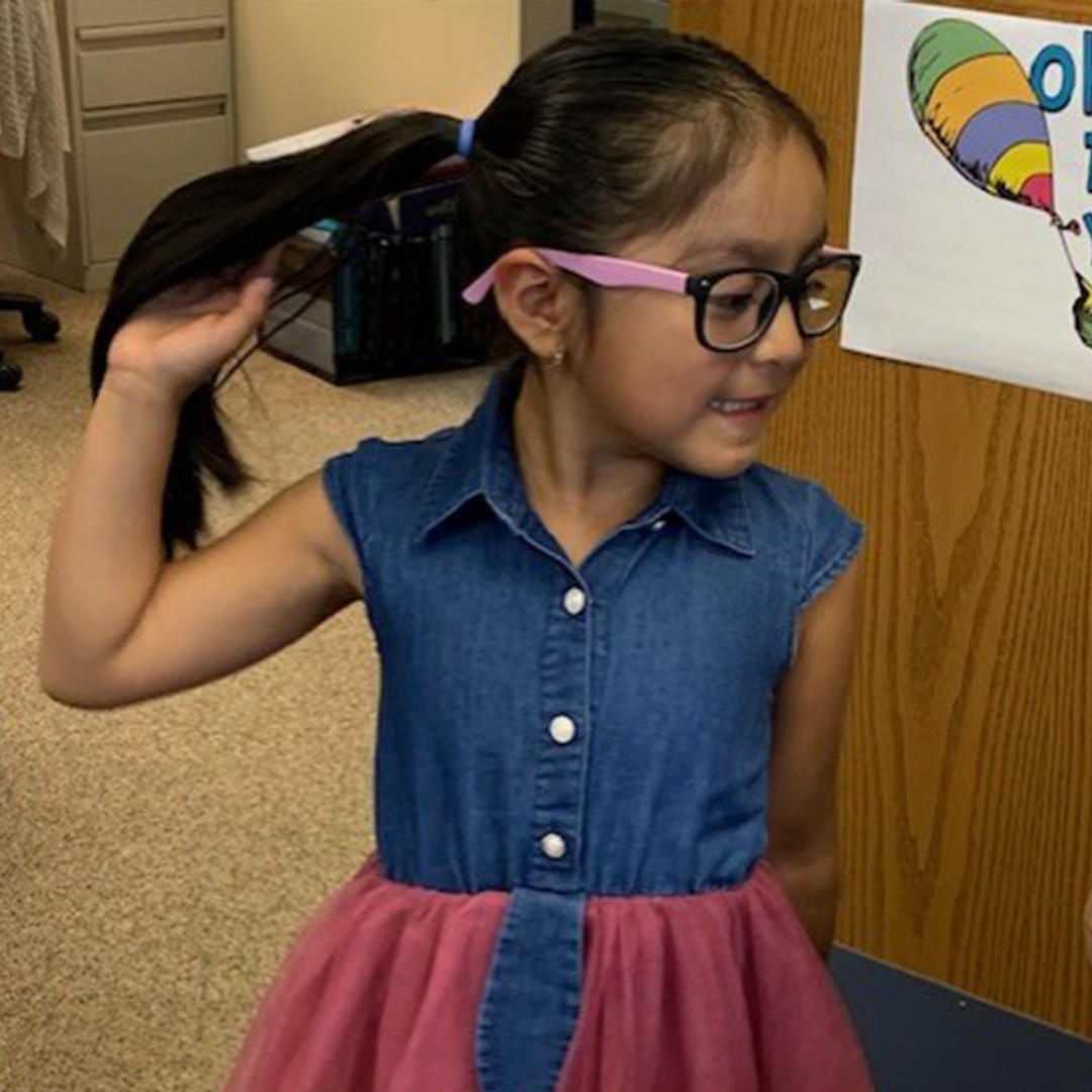 A young girl wearing a blue denim collared shirt flips her hair.