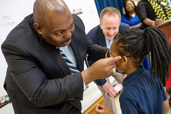 Interim Jackson Public Schools Superintendent Dr. Fredderick Murray helps a child with her new glasses, May 2017.