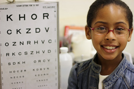 Girl in new glasses next to eye chart