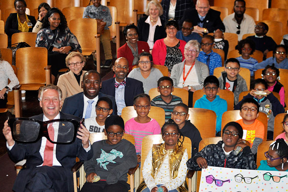 Governor Terry McAuliffe holds a large pair of glasses at the Vision To Learn kickoff event in Richmond, October 2017. Also sitting with some of the children who received glasses are Mayor Levar Stoney, Secretary of Education Dr. Dietra Trent, Interim Superintendent Thomas Kranz, Anne Holton, and other guests.