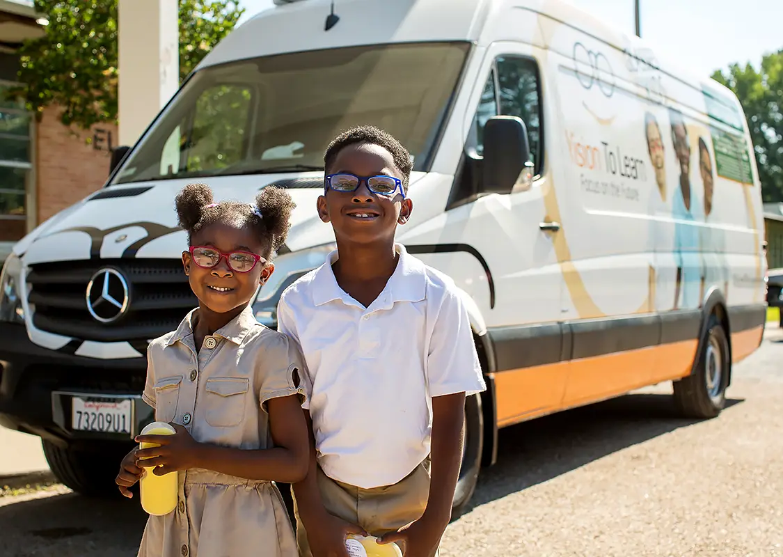 Two children with new glasses in front of mobile clinic